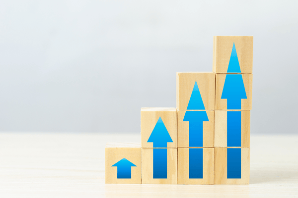 Blok kayu dan panah biru ke atas, melambangkan pertumbuhan profit dengan leverage - Ultima Markets