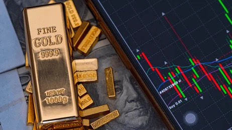 ทองแท่งวางข้างโทรศัพท์ที่แสดงกราฟราคาทองคำในตลาด Forex