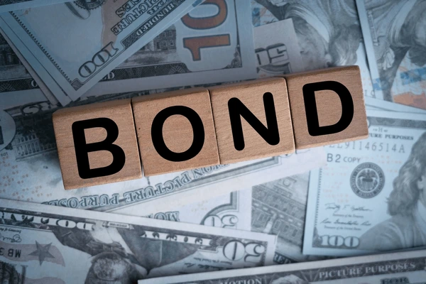 บล็อคไม้ต่อกันเป็นคำว่า BOND วางอยู่บนกองธนบัตร เพื่อสื่อถึงการซื้อขายพันธบัตรรัฐบาลออนไลนแบบ CFD 