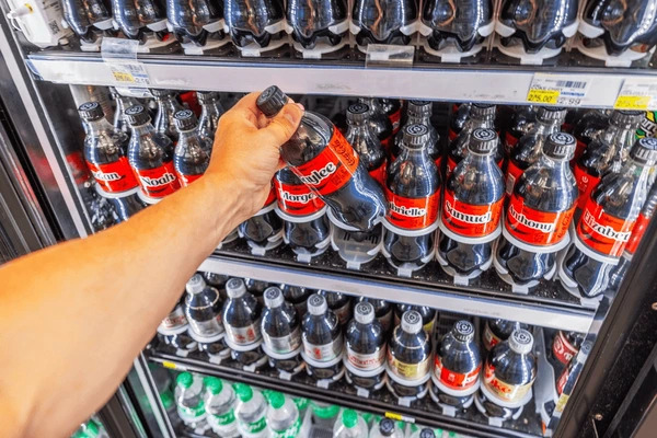 มือผู้ชายกำลังหยิบขวด Caco-Cola ที่อยู่ในตู้แช่เย็น ซึ่งส่งผลโดยตรงต่อราคาหุ้น KO 