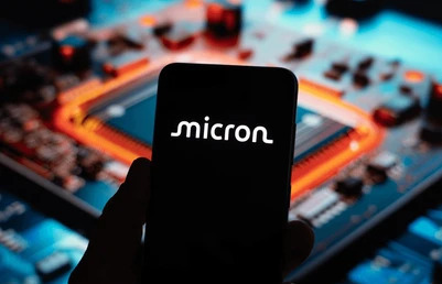 มือกำลังถือโทรศัพท์ที่แสดงโลโก้หุ้น Micron โดยพื้นหลังคือชิปที่ใช้ในอุตสหกรรมเทคโนโลยีต่าง ๆ 