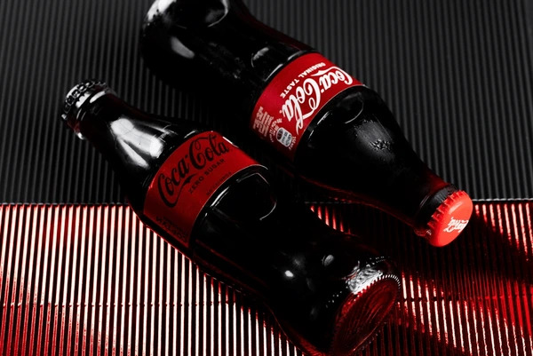 เครื่องดื่ม Coca-Cola 2 ขวดวางอยู่ข้าง ๆ กัน โดยมีทั้งแบบสูตรปกติและแบบน้ำตาลน้อย สื่อถึงการปรับตัวอย่างต่อเนื่อง ส่งผลให้หุ้น KO เติบโต 