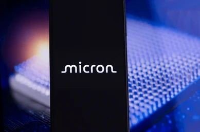 โทรศัพท์ที่หน้าจอเป็นโลโก้บริษัทหุ้น Micron โดยมีพื้นหลังเป็นชิปที่ใช้ในอุตสาหกรรม AI Cloud Computing รถยนต์ไฟฟ้า และอุปกรณ์ IoT 